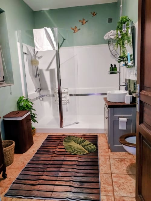 Modern bathroom with sage green walls, walk-in shower, wooden vanity, potted plants, and decorative bird wall art at French