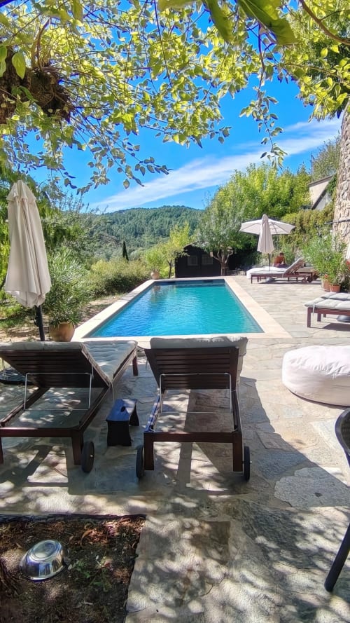Rectangular pool with lounge chairs under pergola, mountains beyond, Cévennes gîte with terrace and gardens