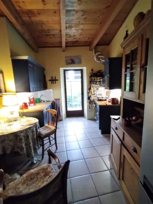 Bright yellow kitchen with exposed wooden ceiling beams, blue cabinetry, tile flooring, and glass doors opening to garden at