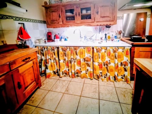 Bright kitchen with red cabinets, sunflower-patterned curtains, and white countertops in French gîte