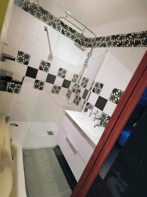 Modern bathroom with black and white patterned tile backsplash, white sink vanity, and shower in French gîte