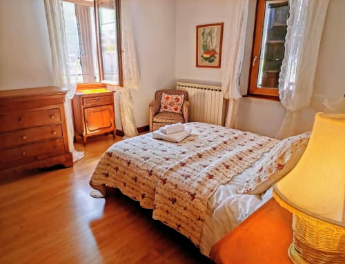 Rustic bedroom in French gîte with wooden furniture, floral bedding, and mountain views in Cévennes