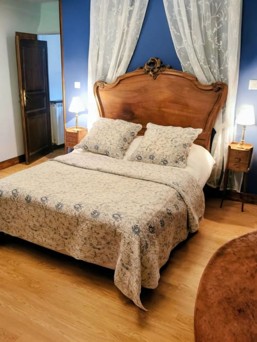 Elegant bedroom with carved wooden headboard, patterned bedding, and sheer curtains in French Cévennes gîte