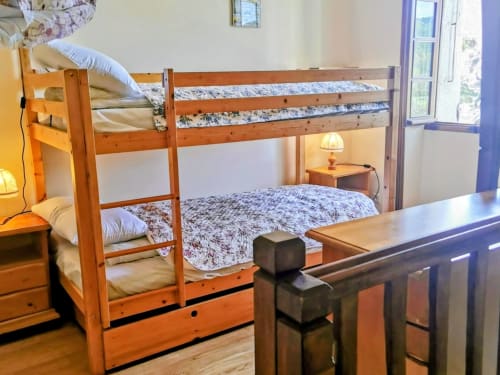 Wooden bunk beds with patterned bedding in a bright cottage bedroom with mountain views and wooden furniture in Cévennes,
