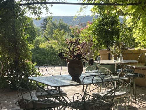 Terrasse extérieure du Clos Bb avec mobilier en fer forgé, plantes fleuries et vue sur les montagnes à Saint-Cyr sur Mer