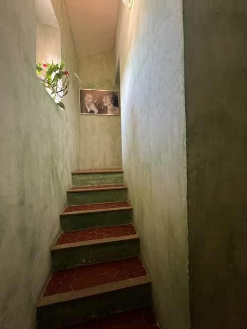 Escalier étroit du Clos Bb aux marches carrelées rouge et vert, murs blancs, plante suspendue et photo encadrée à Saint-Cyr-sur-Mer