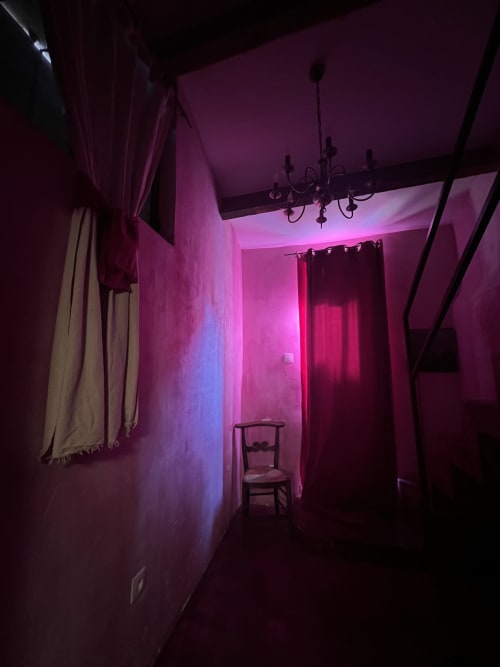 Chambre intime du Clos BB à Saint-Cyr sur Mer avec éclairage néon rose, lustre et chaise en bois
