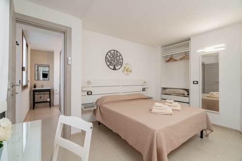 Modern bedroom at Short Let's Olbia with beige bedding, white headboard, ensuite bathroom, and contemporary décor in Olbia,