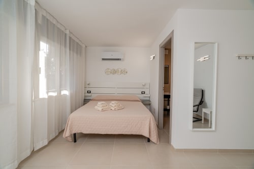 Modern bedroom at Short Let's Olbia with queen bed, pink bedspread, white curtains, and ensuite bathroom access in Olbia,