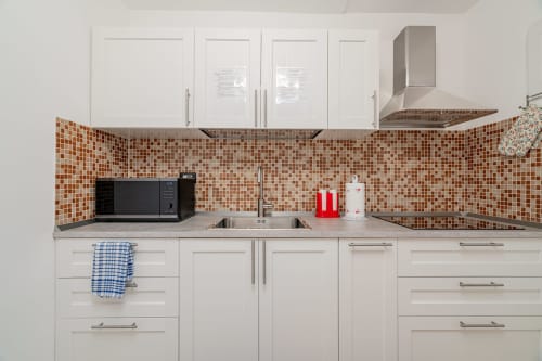 Modern white kitchen with brown mosaic backsplash, stainless steel range hood, and sink at Short Let's Olbia