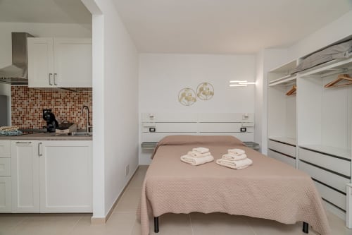 Modern studio bedroom at Short Let's Olbia with kitchenette, bed with folded towels, and wardrobe in Olbia