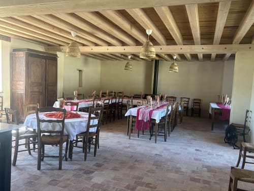 Salle à manger rustique à la Cour Du Liège avec poutres en bois, tables dressées aux nappes rose et luminaires suspendus tissés