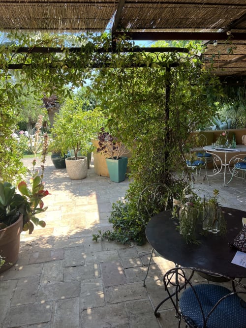 Patio lussureggiante della Clos B&B a Saint-Cyr sur Mer con pergolato ricoperto di rampicanti, vasi di piante e sedute in ferro battuto