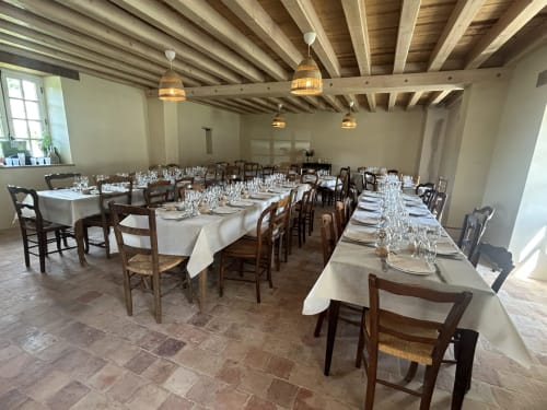 Salle à manger élégante à la Cour Du Liège avec poutres apparentes, tables dressées et chaises rustiques à Baugé-en-Anjou