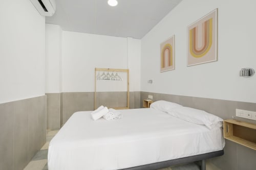 Moderno dormitorio doble en Pensión Castil Granada con ropa de cama blanca, baño compartido, arte geométrico en las paredes y suelo de baldosas.