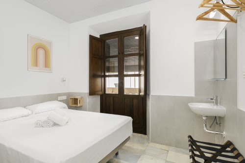 Luminosa habitación doble con baño compartido en Pensión Castil Granada, con ropa de cama blanca, puertas de madera oscura y vistas a la ciudad