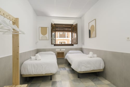 Dos camas individuales en una habitación doble luminosa de Pensión Castil Granada, con vistas a la ciudad a través de persianas de madera y baño compartido