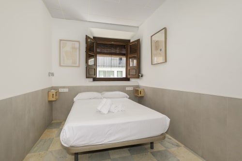 Dormitorio individual compacto con ropa de cama blanca en Pensión Castil Granada, baño compartido, contraventanas de madera y