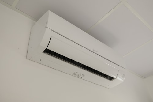 Unidad de aire acondicionado tipo split blanca montada en el techo de una habitación de hotel en Granada con paredes y techo blancos