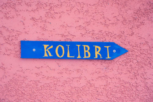 Panneau flèche bleu avec texte doré « KOLIBRI » sur mur rose texturé du gîte Le Nid De Bellemont, Trois-Rivières