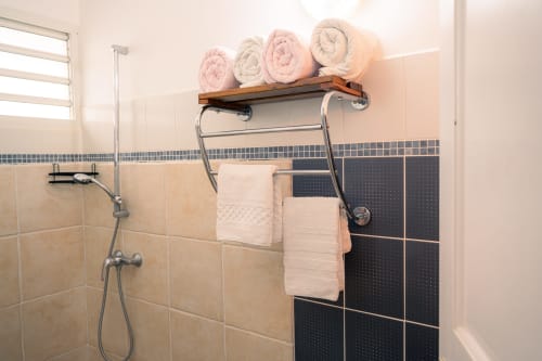 Salle de bain moderne avec serviettes rose et crème roulées, étagère en bois et accents de carrelage noir au gîte Le Nid De Bellemont