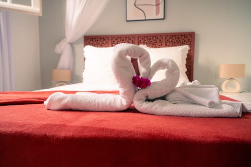Cygnes blancs en serviette avec fleur rose sur courtepointe rouge, gîte Le Nid De Bellemont, Trois-Rivières