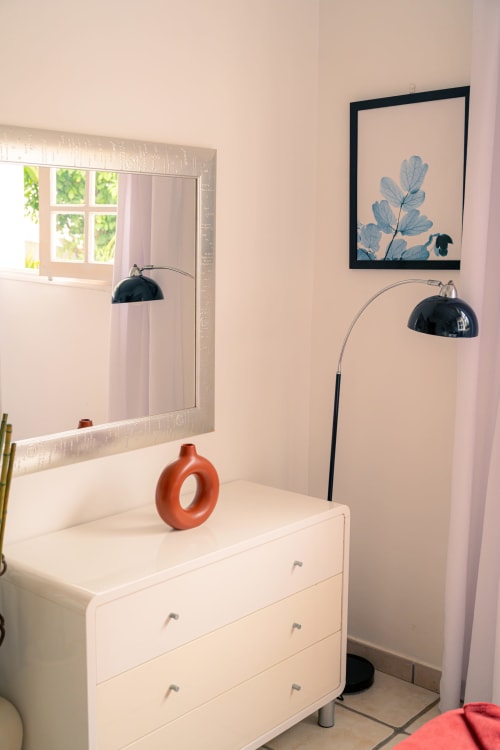 Chambre moderne avec commode blanche, miroir, lampadaire arc et décoration murale botanique au gîte Le Nid De Bellemont à Trois-Rivières