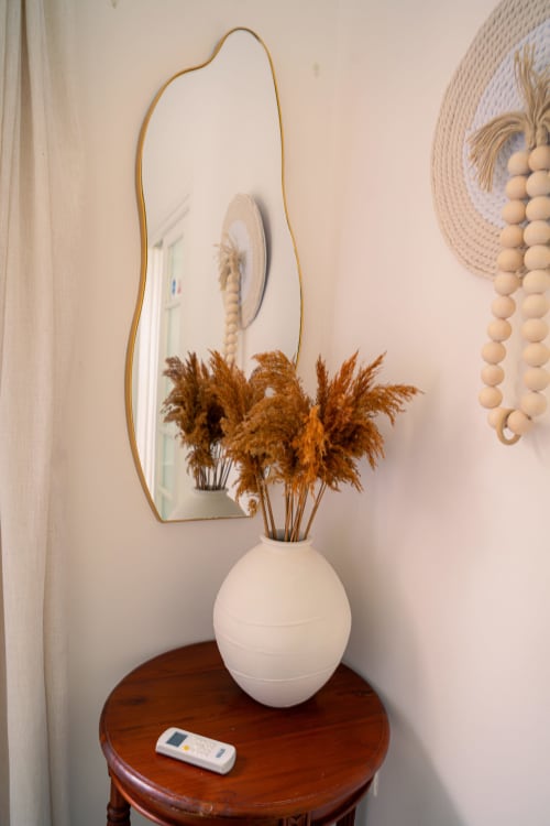 Coin chambre élégant du Nid De Bellemont avec herbes de la Pampa séchées en vase blanc, miroir or courbe et table de nuit en bois