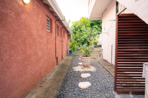 Étroit passage entre les bâtiments en terre cuite et blanc du gîte Le Nid De Bellemont, Trois-Rivières Guadeloupe, avec des pots