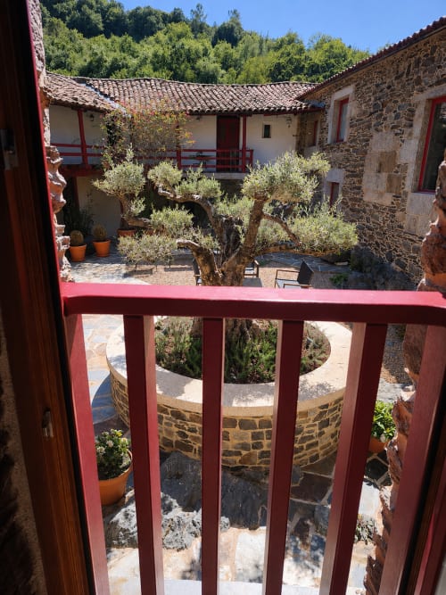 Vista del patio desde el balcón de Casa Grande de Covas con olivos, edificios de piedra y barandillas de madera roja en Taboada, Lugo