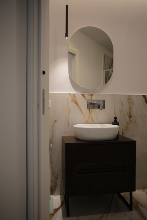 Bagno moderno presso Totonno's Rooms a Tropea con specchio ovale, lavabo bianco, vanità nera e dettagli in marmo