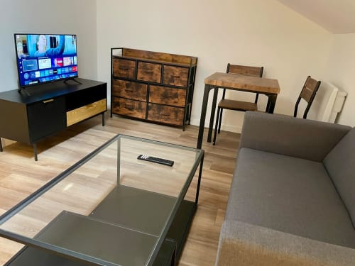 Studio de l'Hôtel d'Angleterre Vittel avec canapé gris, TV, table à manger, mobilier en bois et kitchenette