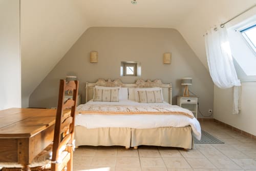 Chambre mansardée lumineuse à la Ferme de Kervihern avec murs beige, literie crème, mobilier bois et velux