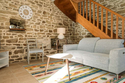 Séjour aux murs en pierre à la Ferme de Kervihern B&B à Locoal-Mendon avec canapé gris, escalier en bois et tapis coloré