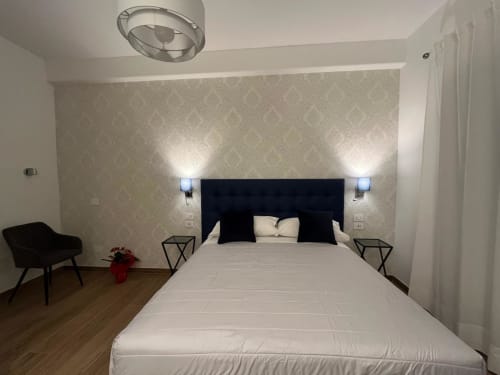 Camera moderna della Maritza Guest House Roma con testata nera, biancheria bianca, carta da parati decorativa e vista sulla città