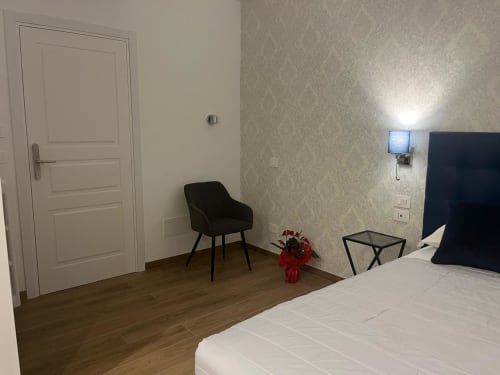 Camera moderna della Maritza Guest House a Roma con porta bianca, sedia nera, fiori rossi e pavimento in legno