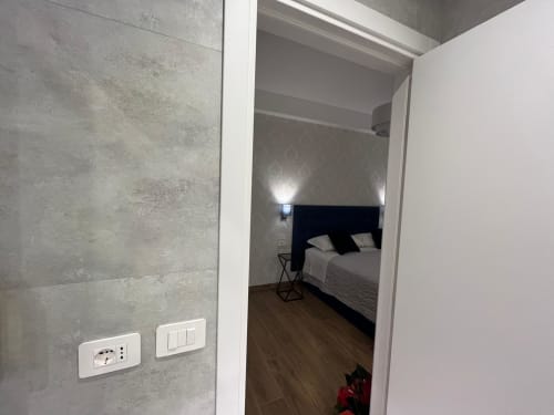Ingresso della camera da letto della Maritza Guest House a Roma con letto dal testata scura e interruttori moderni su parete in rilievo