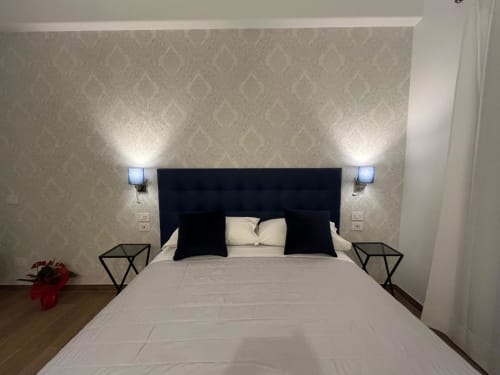 Camera moderna alla Maritza Guest House Roma con testata nera, biancheria bianca, carta da parati decorativa e applique murali