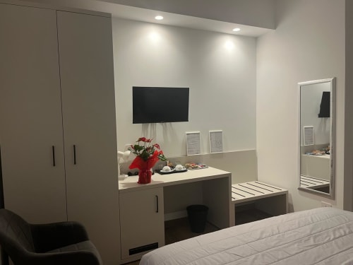 Camera moderna della Maritza Guest House a Roma con armadio incorporato, scrivania con specchio e fiori, TV e specchio a figura intera
