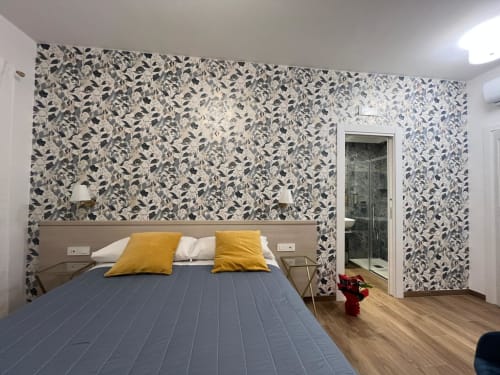Camera moderna della Maritza Guest House Roma con carta da parati decorata, letto blu, cuscini gialli e vista sulla città