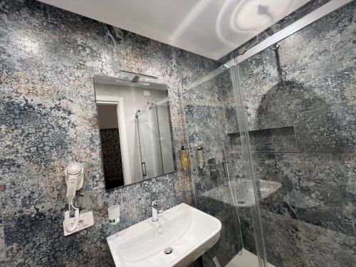 Bagno moderno della Maritza Guest House Roma con rivestimenti in granito, lavabo bianco, specchio e doccia in vetro
