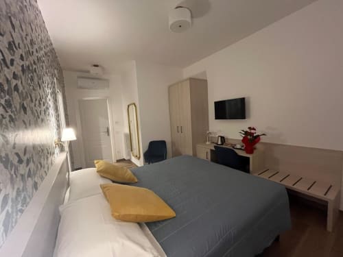 Camera moderna alla Maritza Guest House Roma con letto grigio, cuscini gialli, TV a parete e parete decorativa con motivi