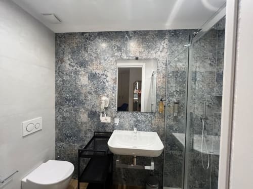 Bagno moderno alla Maritza Guest House Roma con piastrelle grigie strutturate, lavabo bianco, toilet e box doccia in vetro