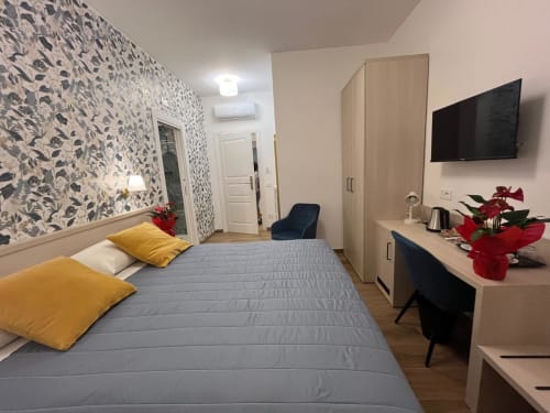 Camera moderna alla Maritza Guest House Roma con carta da parati floreale, cuscini gialli, TV, scrivania con fiori e vista sulla città