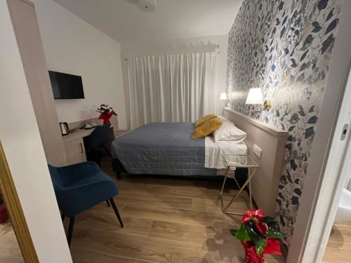 Camera moderna alla Maritza Guest House di Roma con letto grigio, sedia blu, carta da parati decorata e vista sulla città