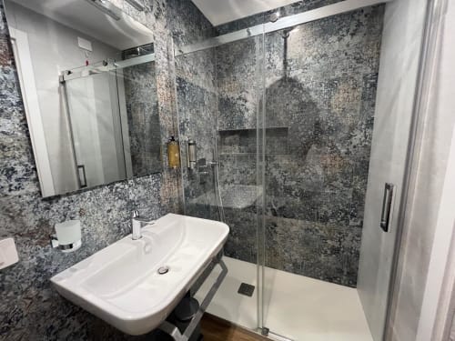 Bagno moderno della Maritza Guest House Roma con piastrelle in pietra grigia, lavabo bianco, box doccia in vetro e specchio