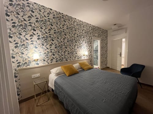 Camera moderna presso Maritza Guest House Roma con carta da parati floreale, letto grigio, cuscini gialli e vista sulla città