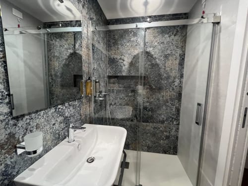 Bagno moderno della Maritza Guest House Roma con doccia in marmo grigio, lavabo bianco e box doccia in vetro