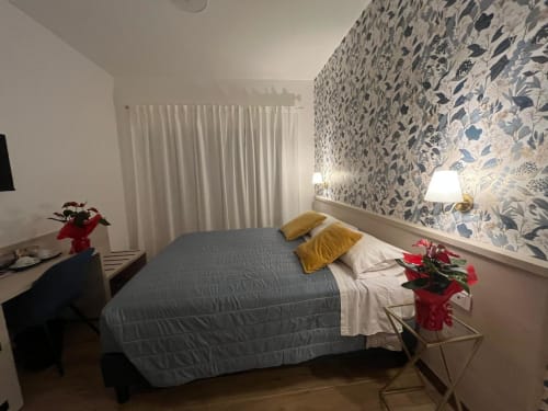 Accogliente camera da letto a Maritza Guest House a Roma con carta da parati decorata, letto grigio, cuscini dorati e fiori rossi