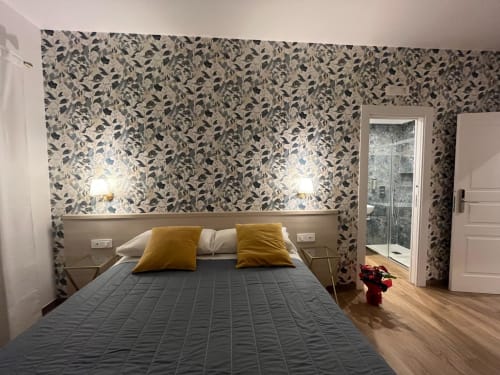 Camera moderna della Maritza Guest House a Roma con carta da parati floreale, letto grigio, cuscini dorati e vista sulla città